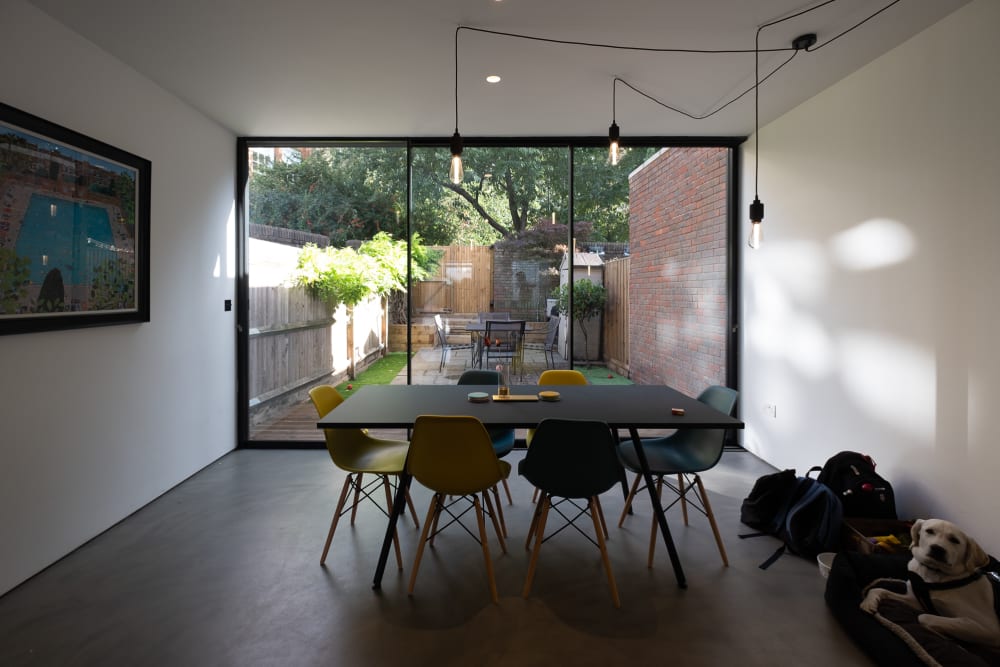 A photo facing straight on in a kitchen, facing out towards a kitchen. There’s floor to ceiling glass windows, and a smart table in the foreground.