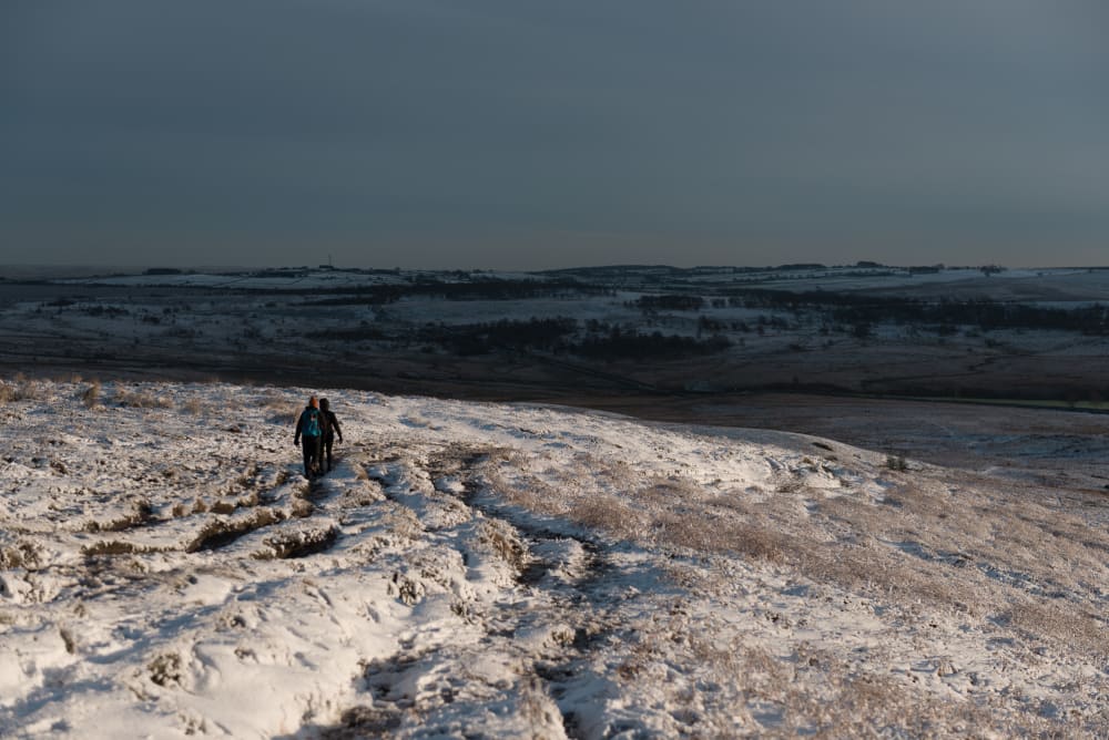 A pair of walkers decend a snow covered hill.