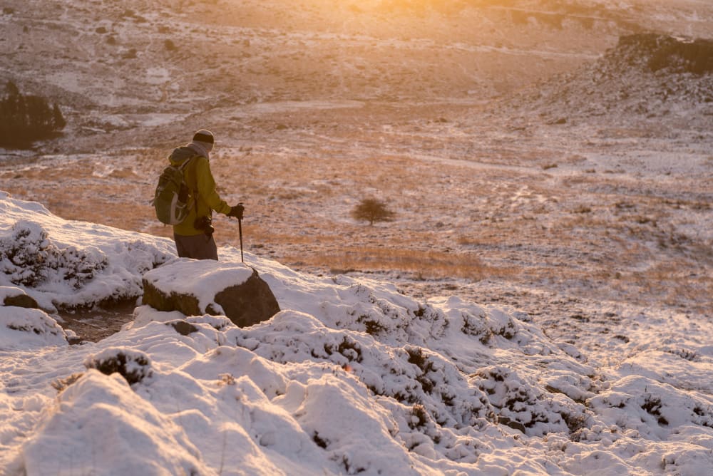 A hiker with hiking pole descends a snow covered hill at sunset.