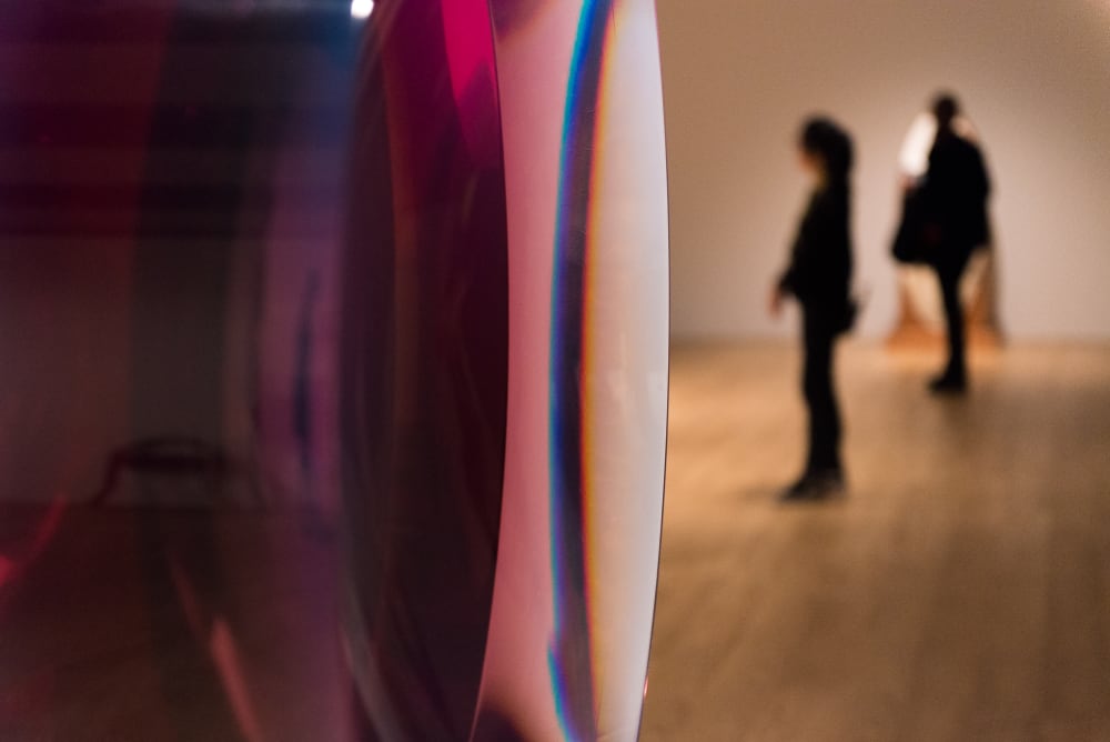 A close macro photo of a translucent dark red and violet object. There are blurred people in the background.