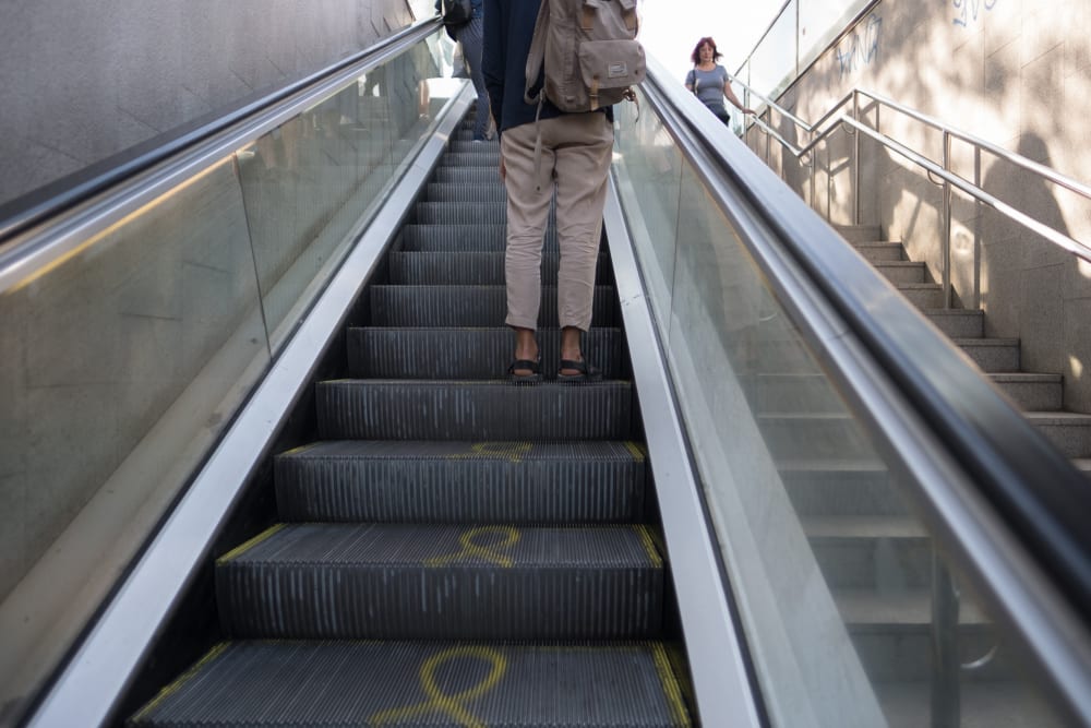 Photo looking up an escalator in to a bright sunny day. There’s someone on the escalator ahead.