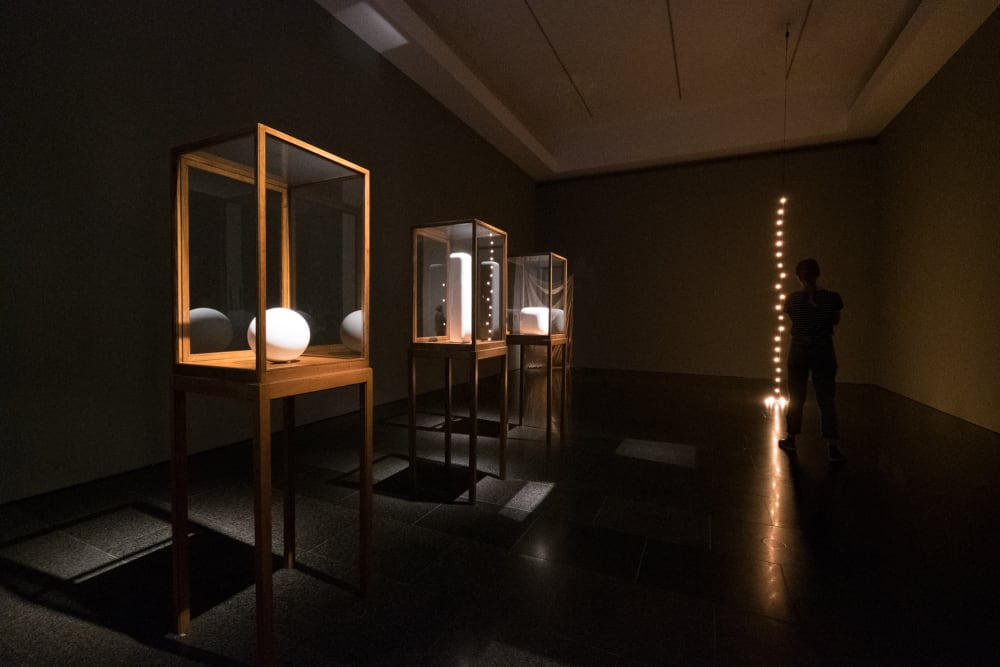 A photo of a dark room with three wooden display cabinets filled with white objects on one side.