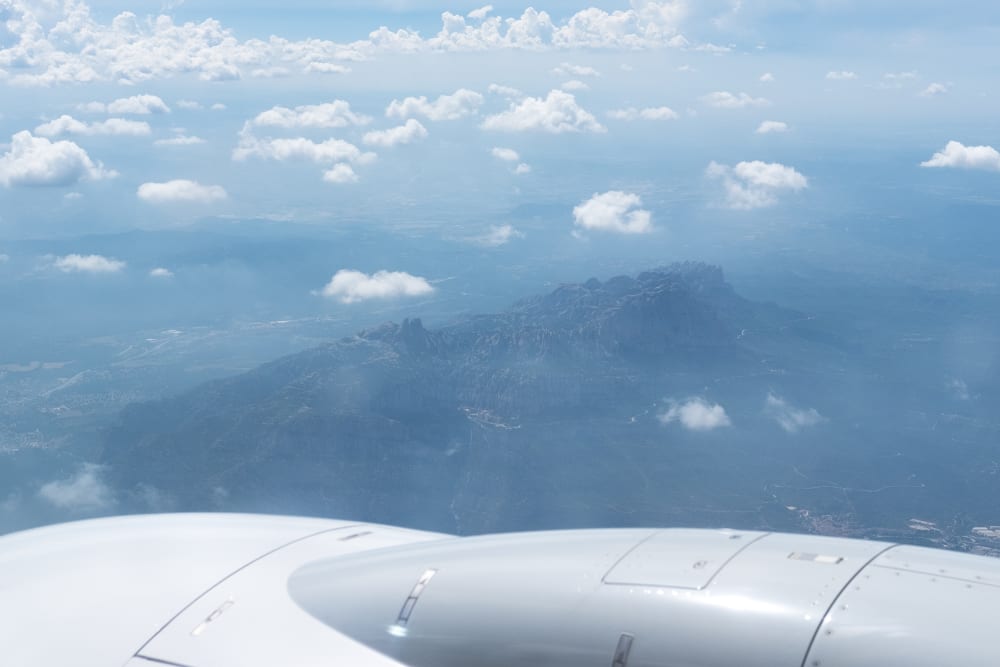 A photo of the Montserrat mountain range taken from an airplane. A plane engine is visible in the foreground.