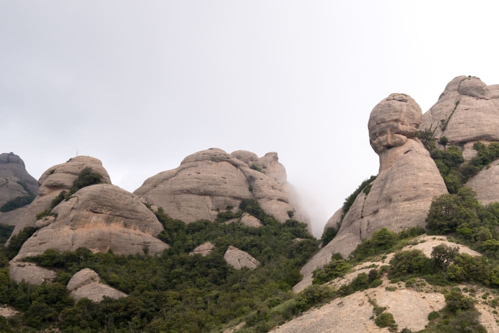 Looking up at the peaks of some mountains in Montserrat. The rocks are bulbous and separated like molten lumps.