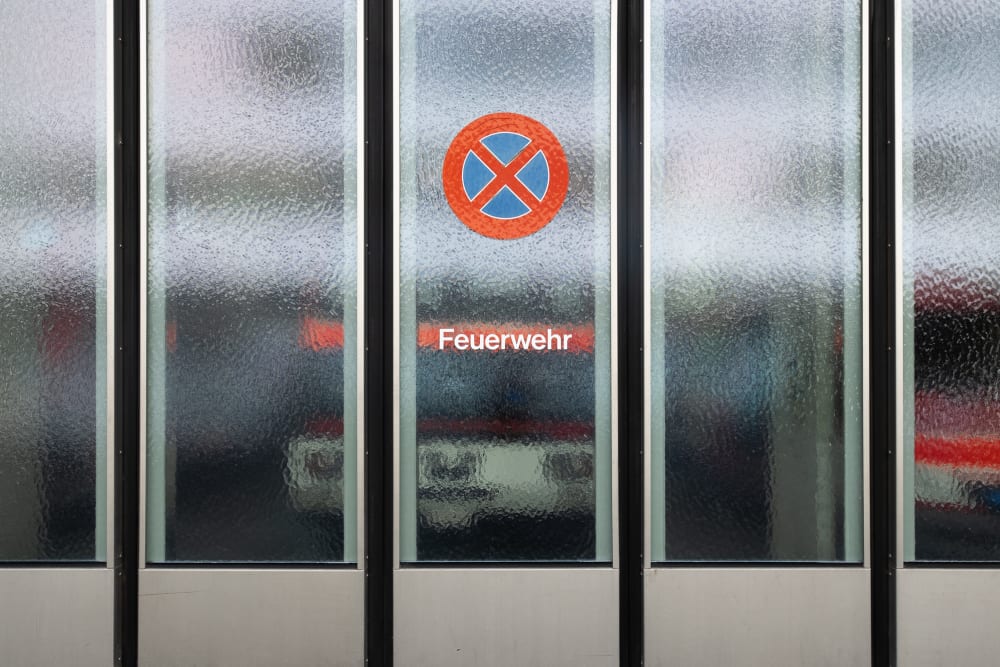 A photo of the frosted glass garage door of a fire station. There’s a sign that reads ‘feuerwehr’ (fire department), and a symbol with a red no entry sign.