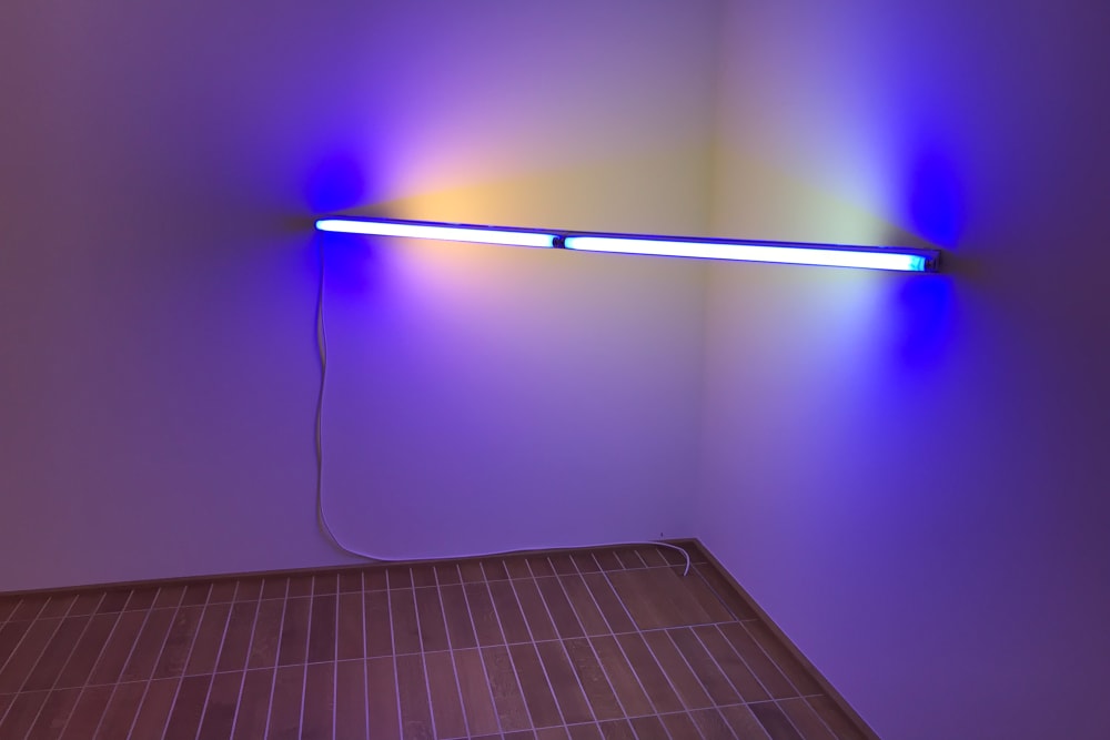 Photo of a light sculpture by Dan Flavin in the Kunstmuseum. The sculpture is a long fluorescent bulb stretching between two walls in the corner of a room. The bulb is the only source of light, and gives of a blue and white light.