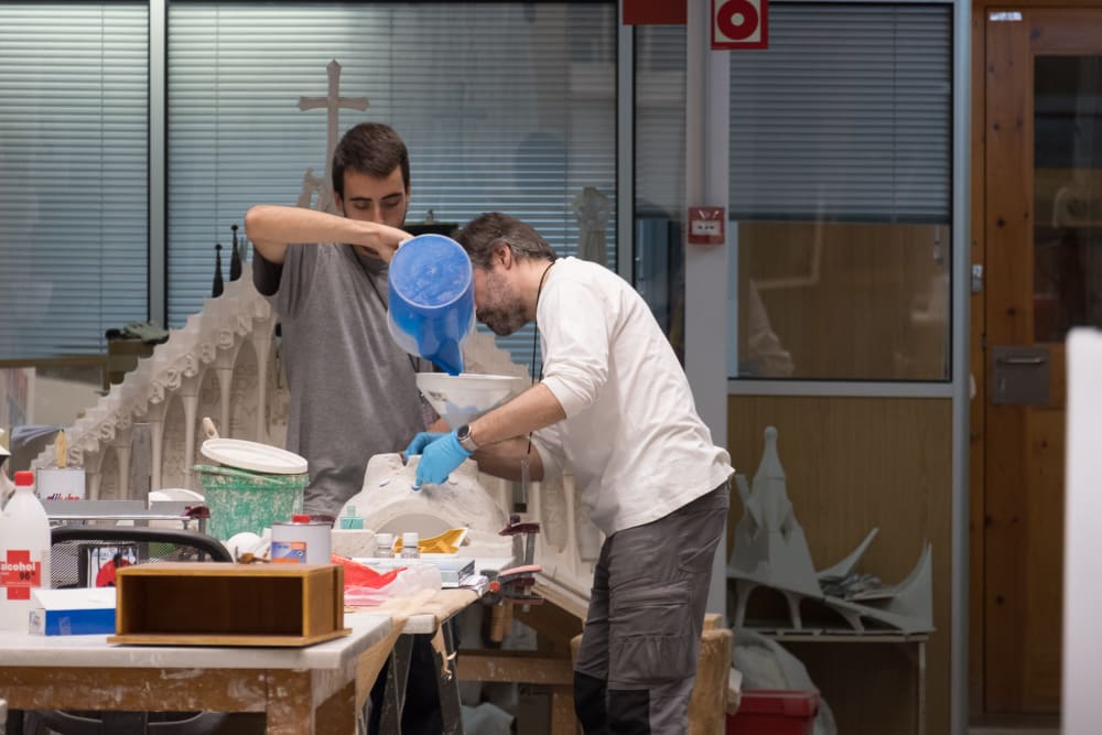 Two model makers pour plaster in to a mould.