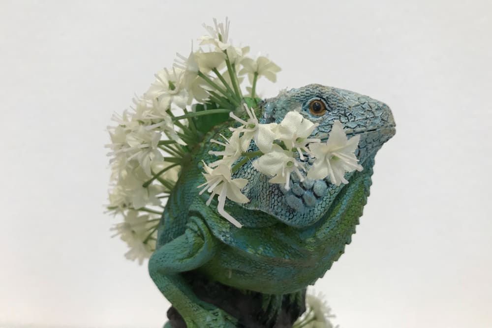 A close photo of a model of a lizard with flowers growing out of it’s back.