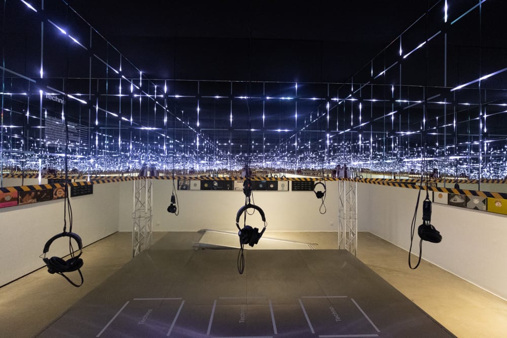 A view inside an art installation at the Vitra Design Museum. There’s mirrors ahead and on the sides creating an infinite loop. The room is dark, but small squares of light repeat.