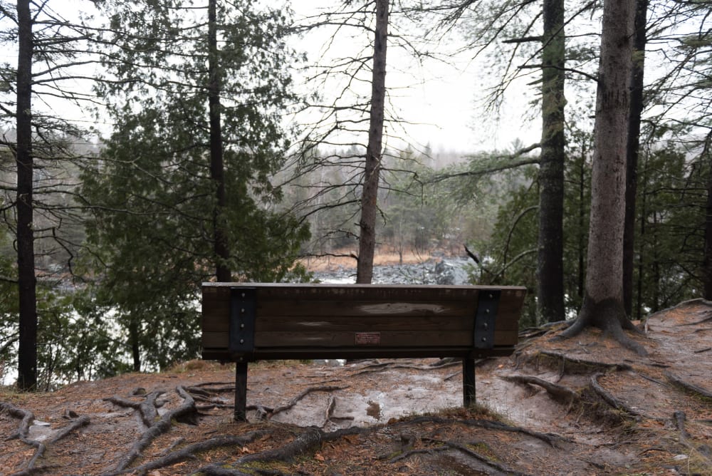 A photo from behind of a park bench overlooking a snowy river.