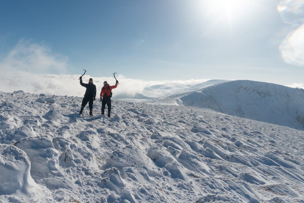 Ed and Chris with axes in the air on a snowy plateau.