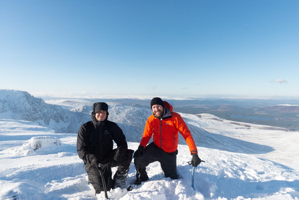 Ed and Chris kneel down with ice axes in hand at the top of Stob Coire an t-Sneachda