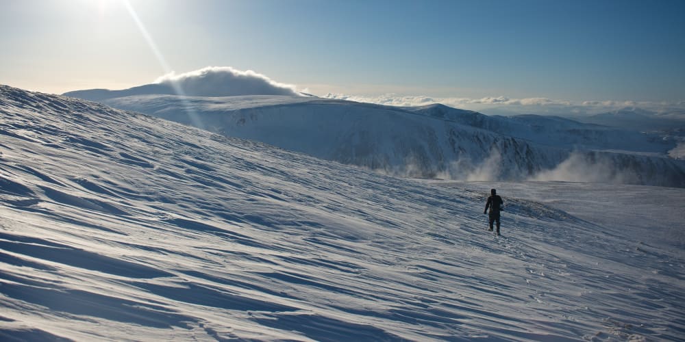 A man descending a snowy hillside in afternoon sun.