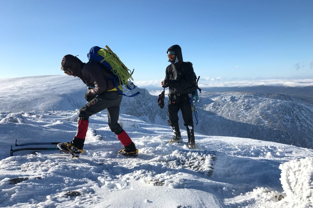 Two climbers in full winter gear at the top of a snowy mountain.