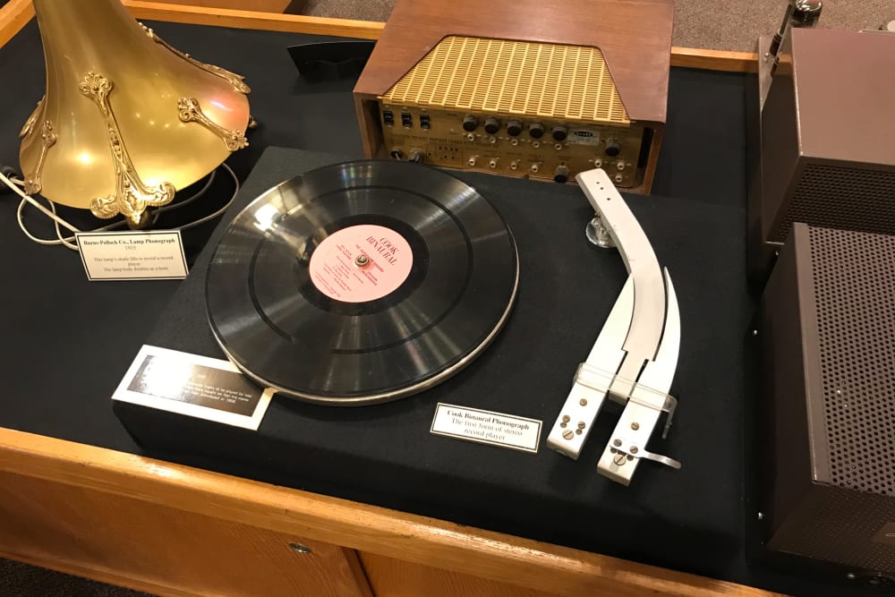 A photograph of a vintage radio player. The player has two reading heads side by side rather than one. The record has two visible tracks.