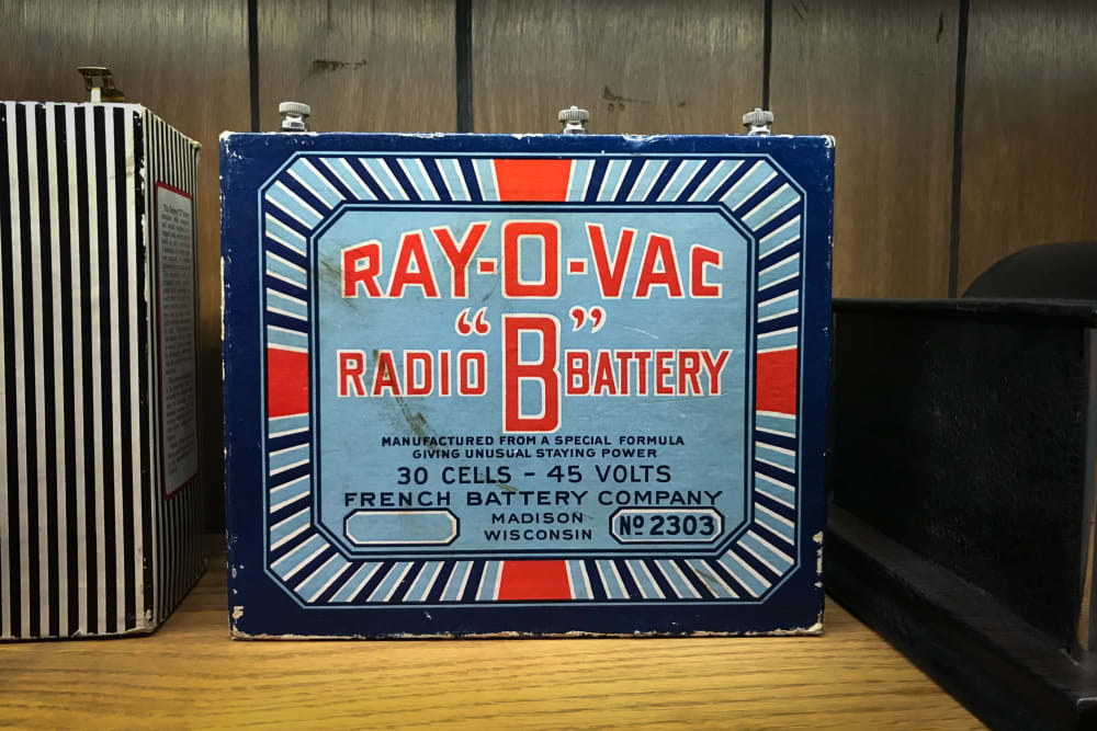 Photo of the front of a vintage radio battery. The battery is brightly coloured with a graphic dark blue, light blue, white and red design. The front text reads “Ray-o-vac radio ‘B’ battery”