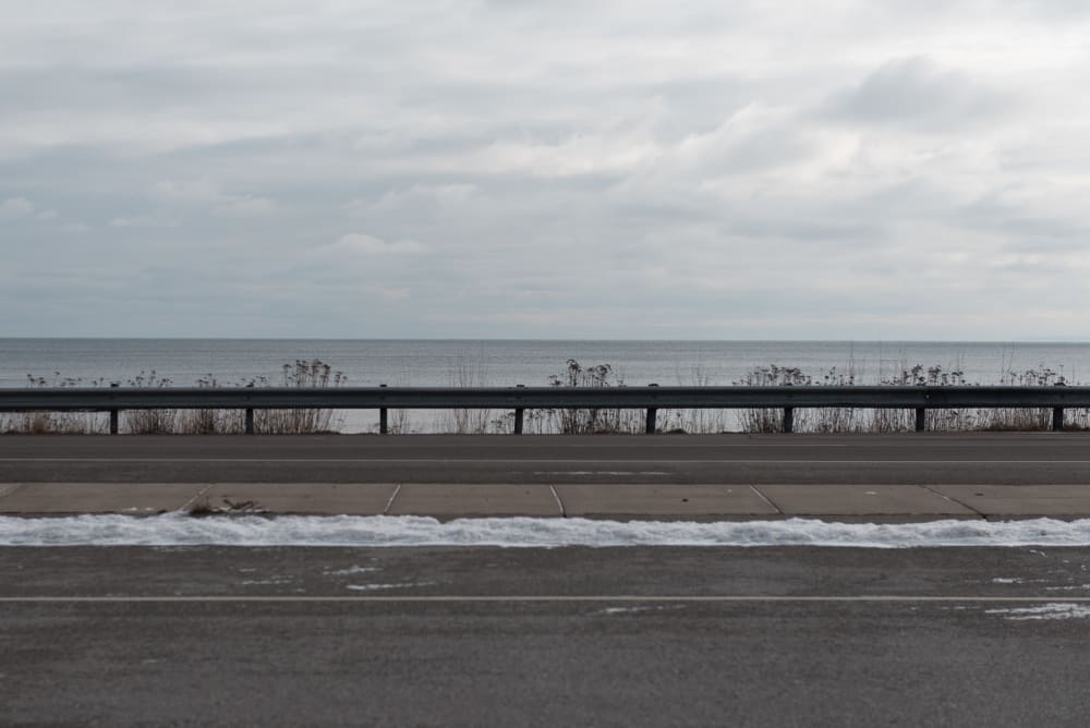 A photo from the side of a highway looking over the side. Lake Superior is in the background.