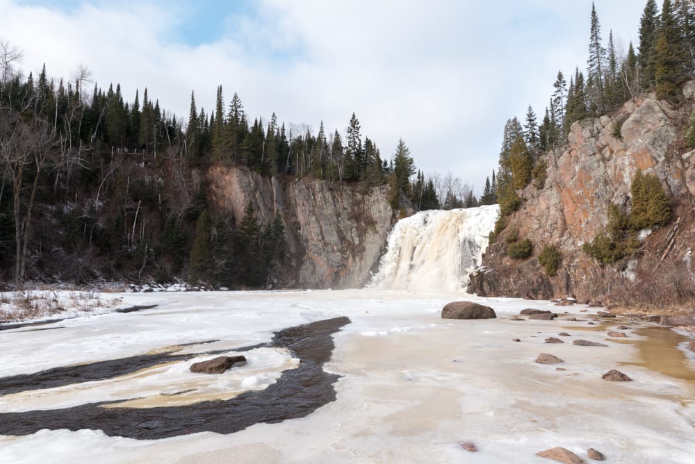 A photo of High Falls taken from the pool at it’s base. The water is partially frozen over.