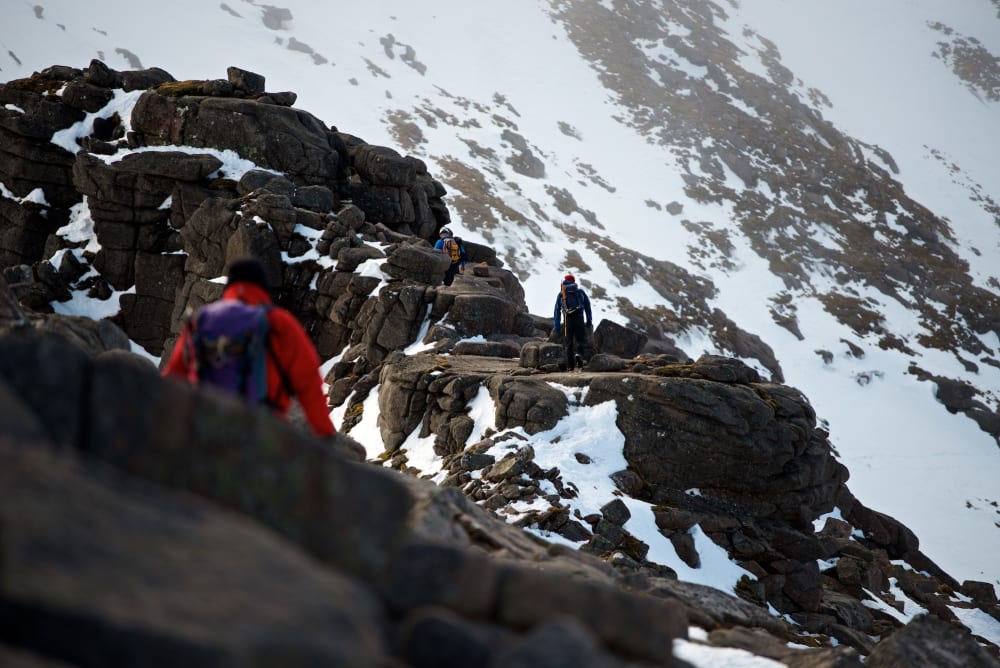 A photo taken facing along Fiacaill ridge. There’s climbers walking along various sections of it, with one in the foreground.