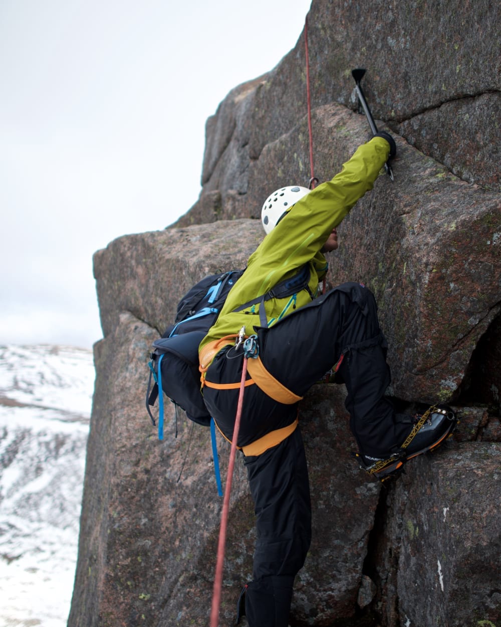 Chris takes a big step out on to an exposed section of Fiacaill ridge. His axe is in a crack providing support.