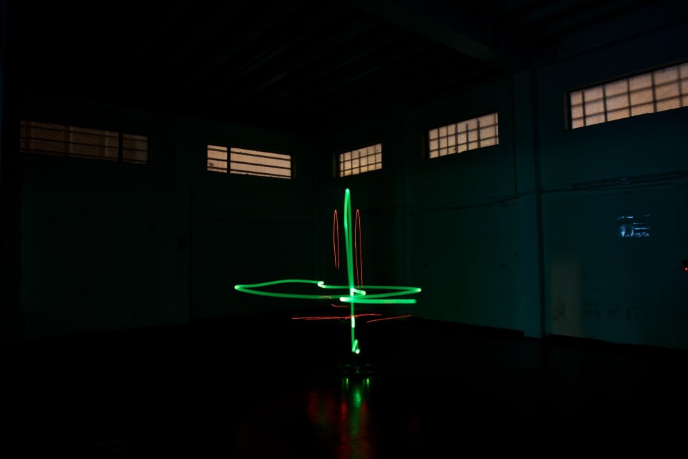 A photo taken in a dark warehouse from below. A green light is in the center in a cross shape.