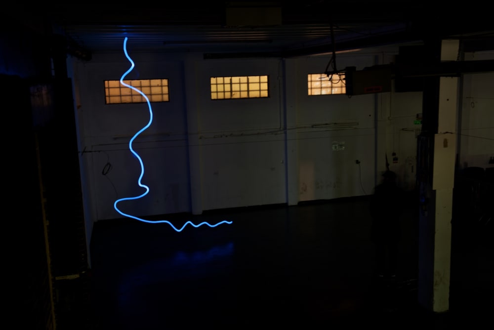 A photo taken in a dark warehouse from above, looking down. There’s a single blue line of light snaking from the floor to the ceiling.