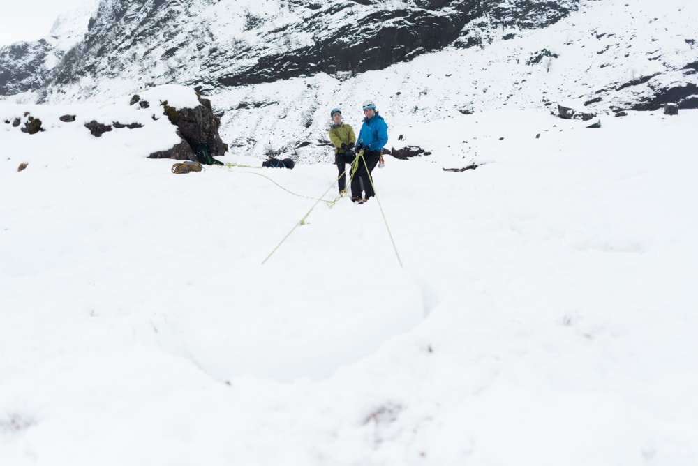 Chris and our guide pull on a length of rope coming towards the camera. The rope runs around a pillar of snow making an anchor.