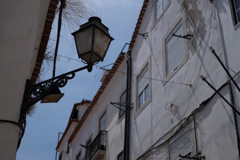 Looking up at a streetlamp in a narrow street. It’s daylight, so the streetlamp isn’t on.