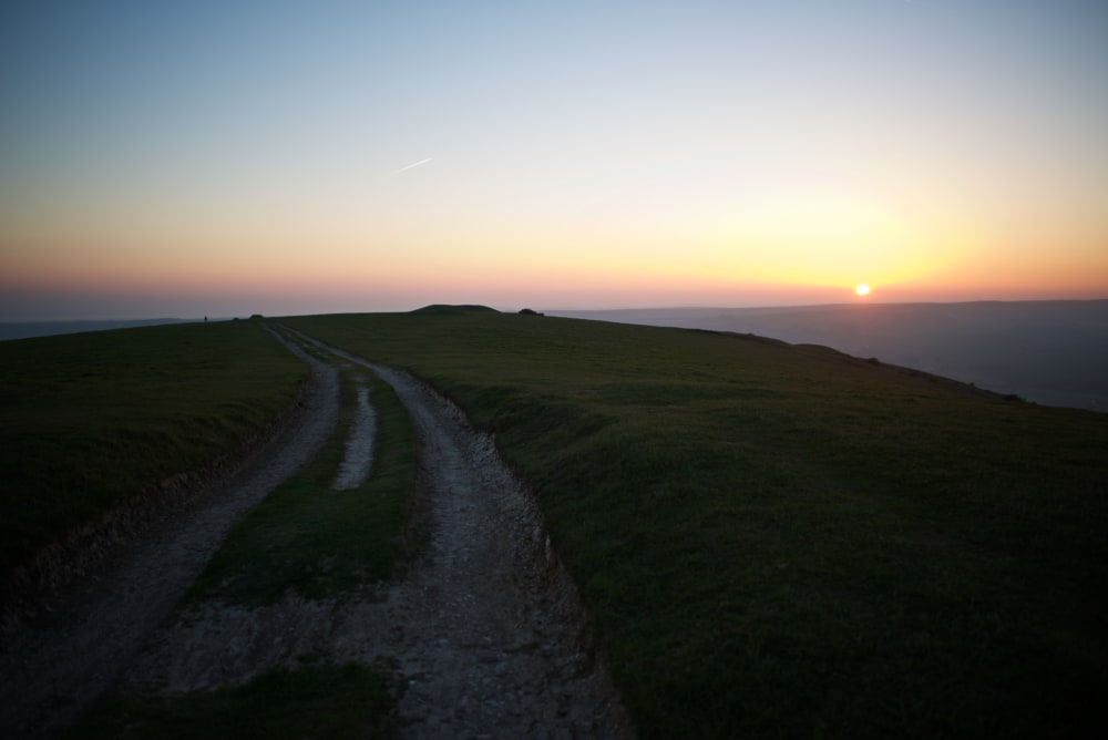 A chalky path recedes in to the distance on a hillside. The sun is just setting on the horizon.