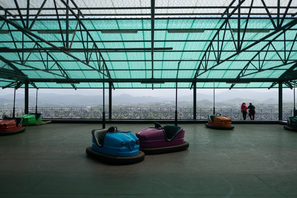 Bumper cars sit unused at the top of a mountain. In the background the city of San Sebastián can be seen below.