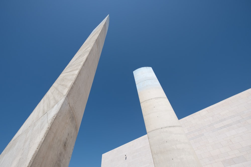 Looking up at two exterior sculptural concrete towers in the Champalimaud Foundation. The towers are light grey in an otherwise deep blue sky.