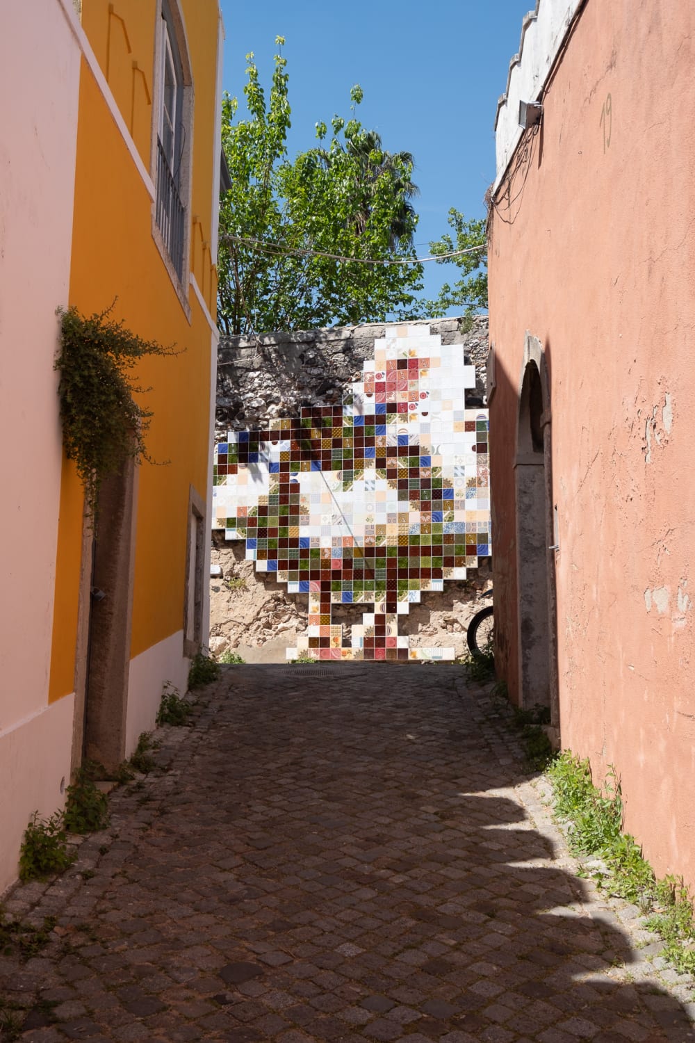 A bright colourful view of an alleyway. The alley ends in a large mosaic.