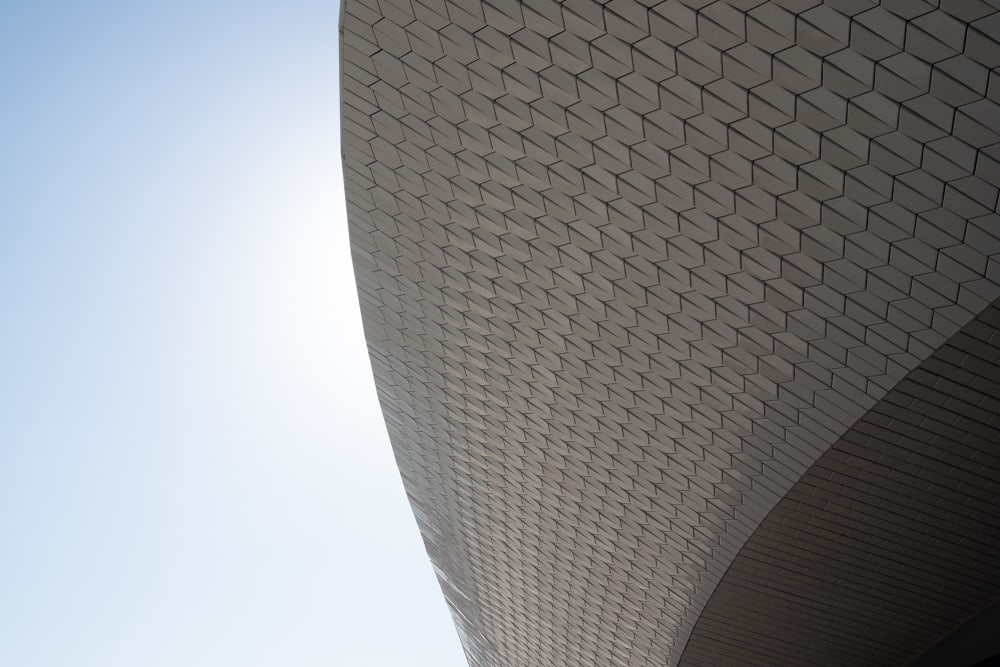 A close cropped detail of the Maat ceiling. the ceiling is in a flowing curved form and covered in small tiles. A cloudless sky can be seen behind.