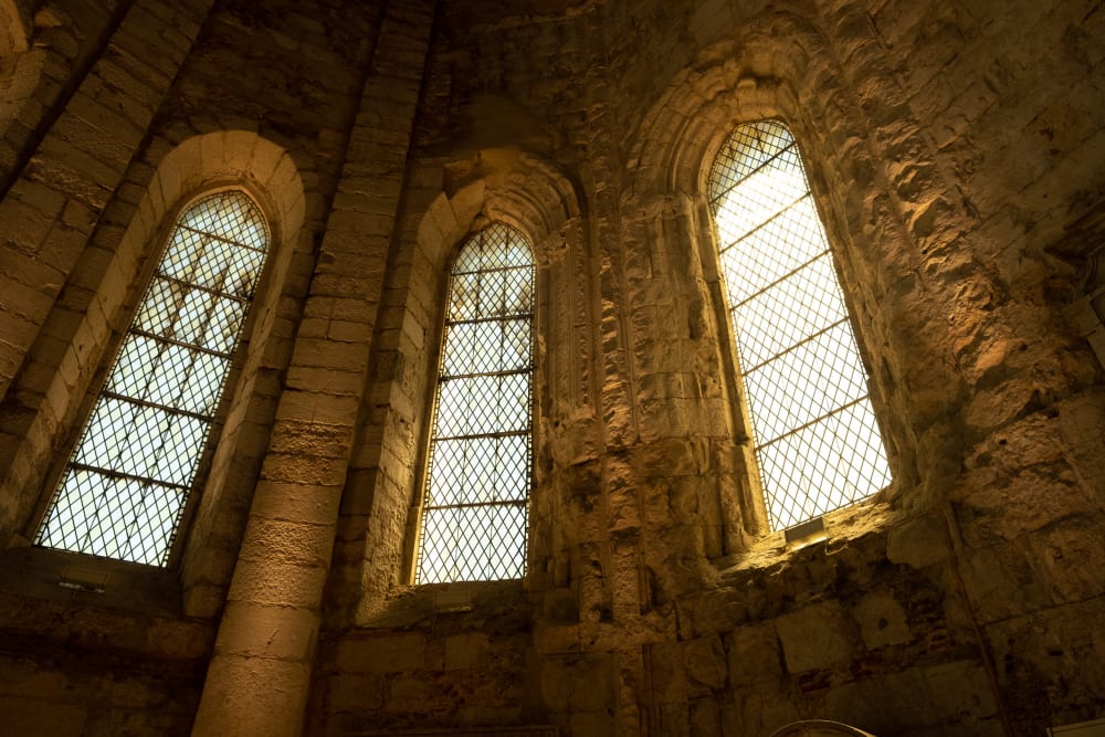 An interior view of three windows in the Carmo Convent - the interior is dark but warmly lit by the three windows.