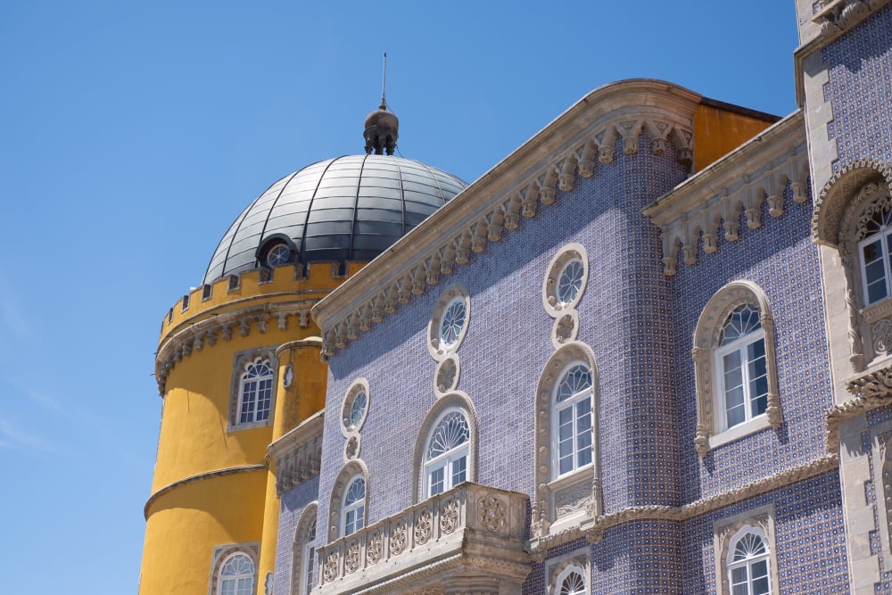 A view of two buildings in the Pena palace. the near building is covered in deep blue tiles with light stone trim. The far building is cylindrical and yellow.