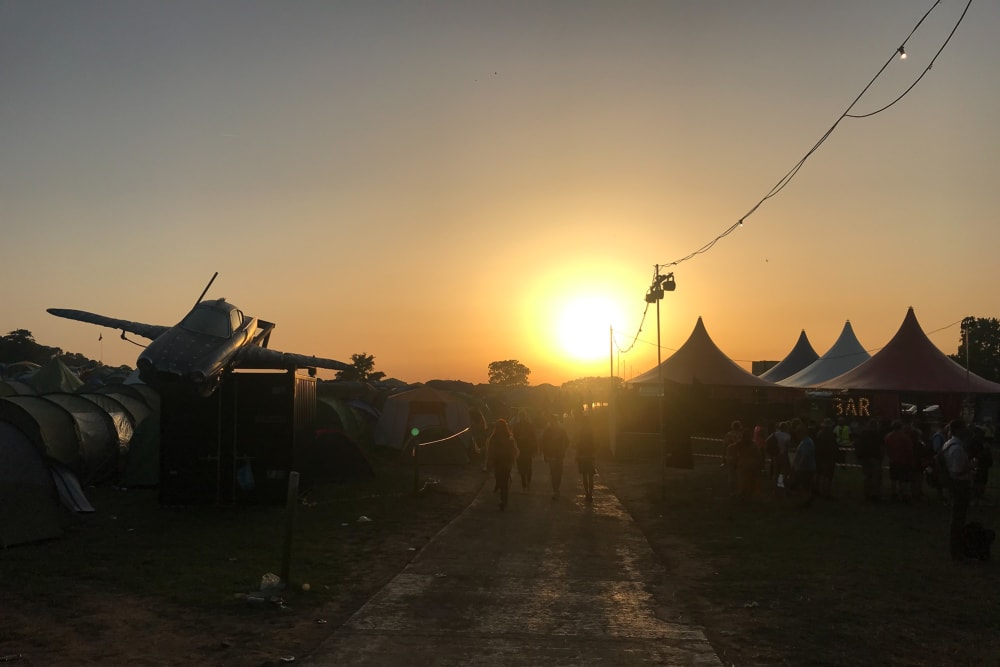 Sunset over Glastonbury. There’s tents on the right and a plane on the left.