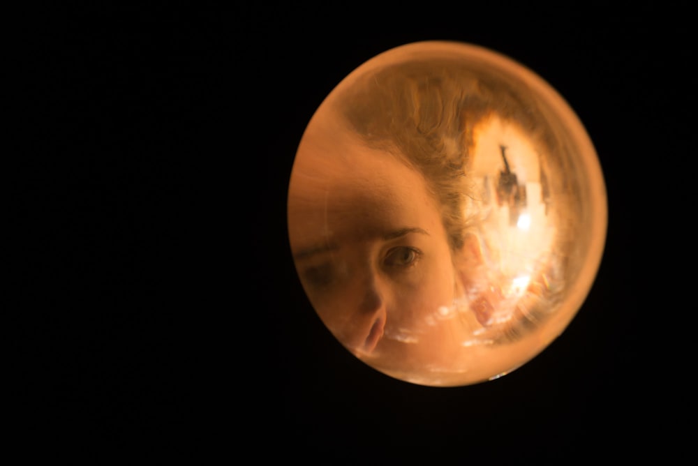 A solid sphere of glass fills the right frame of the photo, set against black. There’s an image of a woman’s face magnified inside the glass.