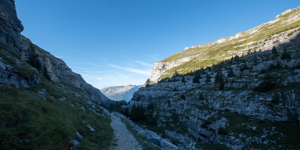 A photo looking down a valley in shadow as the sun sets. The right hand cliff is still lit brightly, in contrast to the dark blue rocks below.