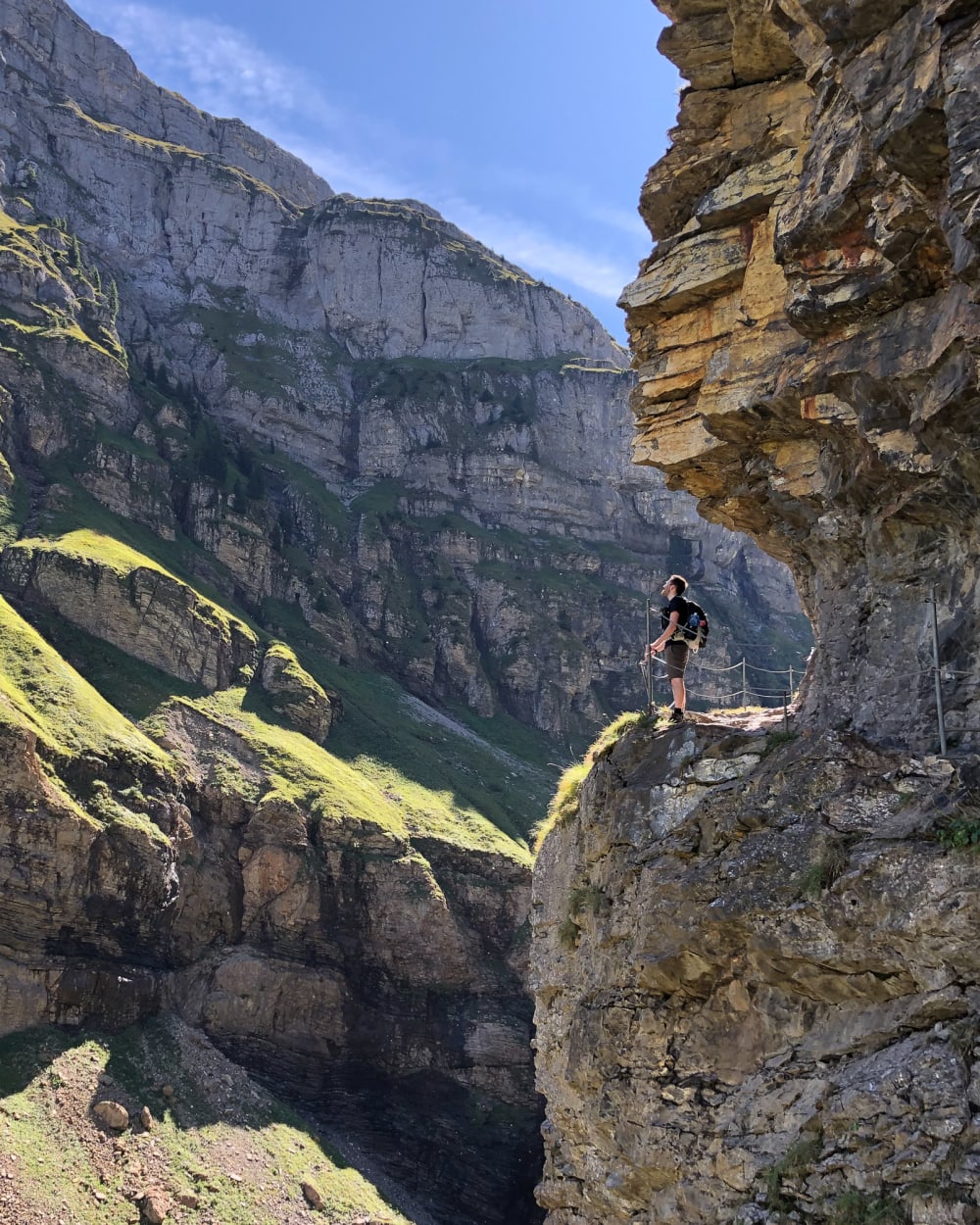 Ed holds a railing as he looks from one side of a steep valley to the other. The side he’s stood on has a near vertical wall of stone, with a path cut out in to it.