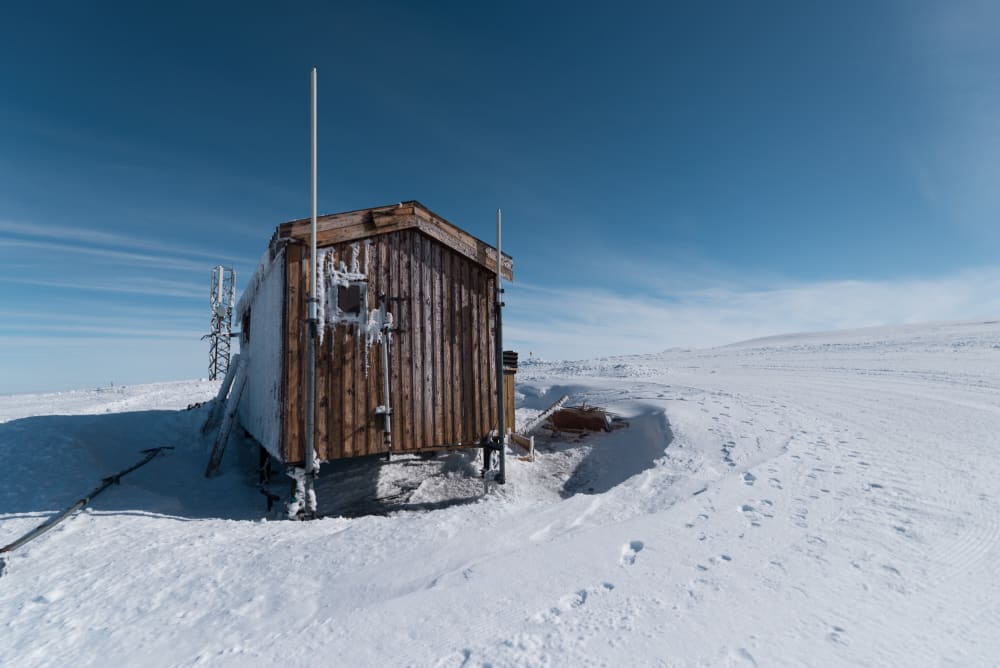 A small wooden shelter on a snowy mountainside with deep blue sky.