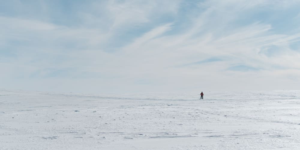 A lone cross country skier on an otherwise flat and snowy plateau.