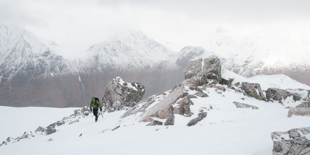 Ed ascending towards the camera. There’s several large boulders partially covered in snow to the right.