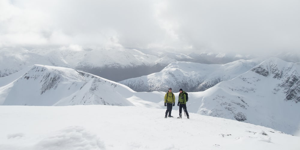 A portrait photo of Chris and Ed on top of a snowy mountain, with several other snowy summits visible behind.