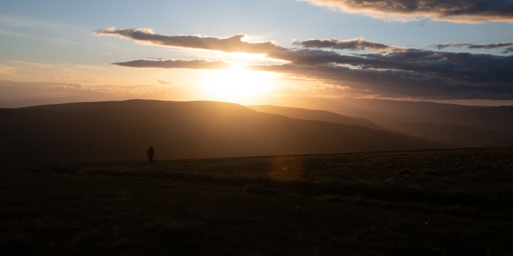 Chris in silhouette against an empty hillside, facing the sun as it sets.