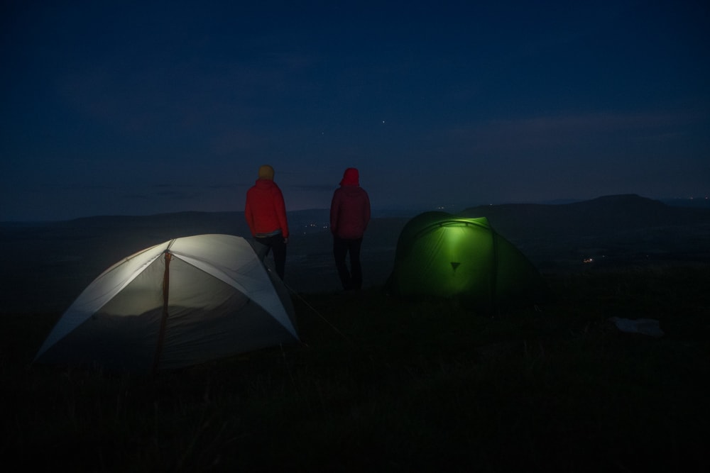Ed and Chris stand still in the dark next to their tents. Each tent glows slightly from within.