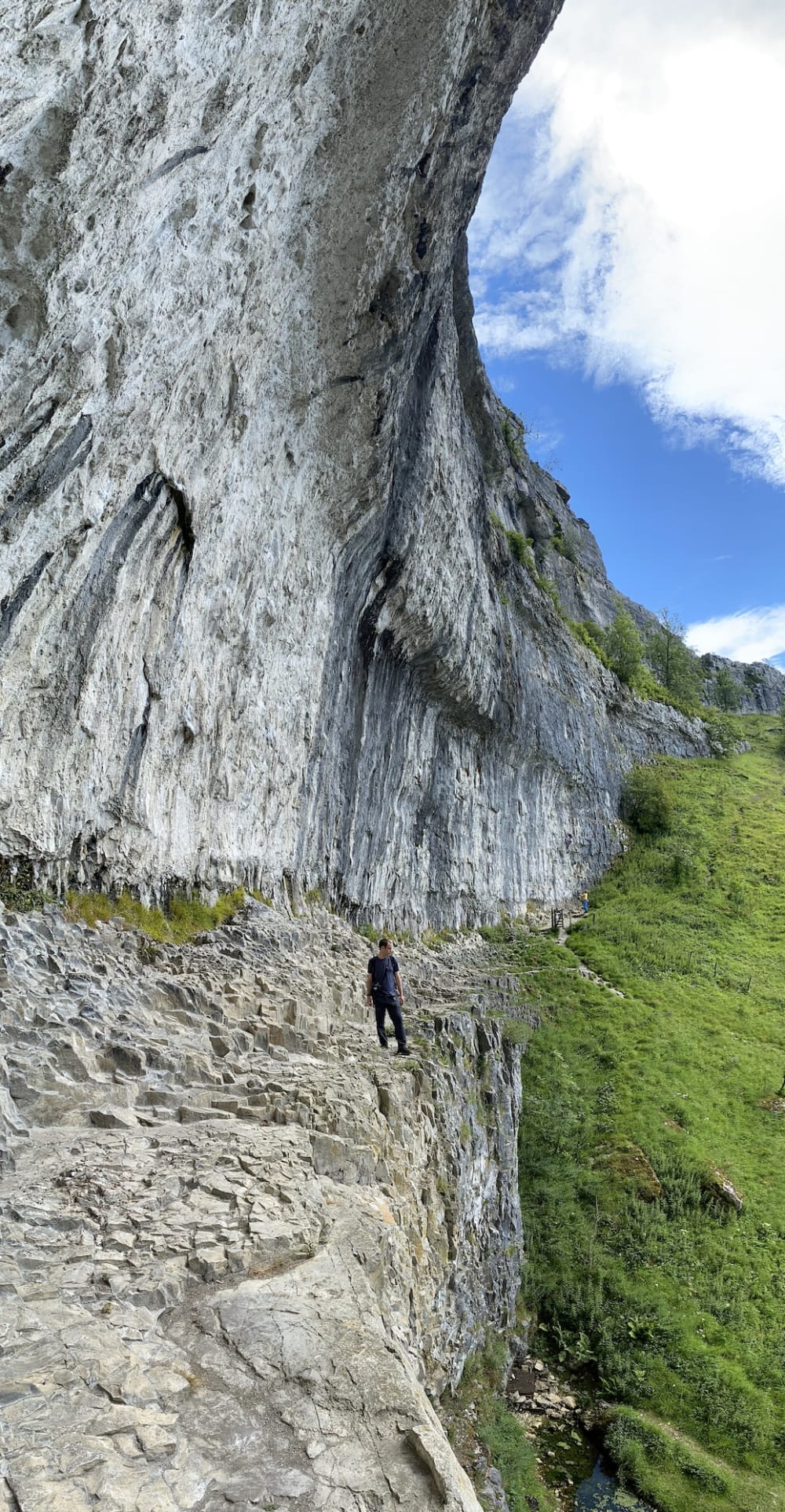 A vertical panorama from the side of Malham Cove. A large rock face looms over Chris.