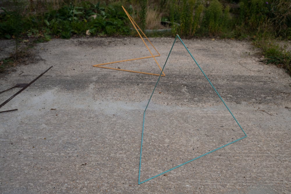 Two coloured geometric metal objects rest on a concrete floor. 