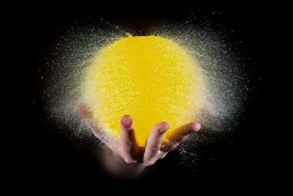 Photo of a water balloon bursting. The balloon is resting on a hand, and lit up like the sun.