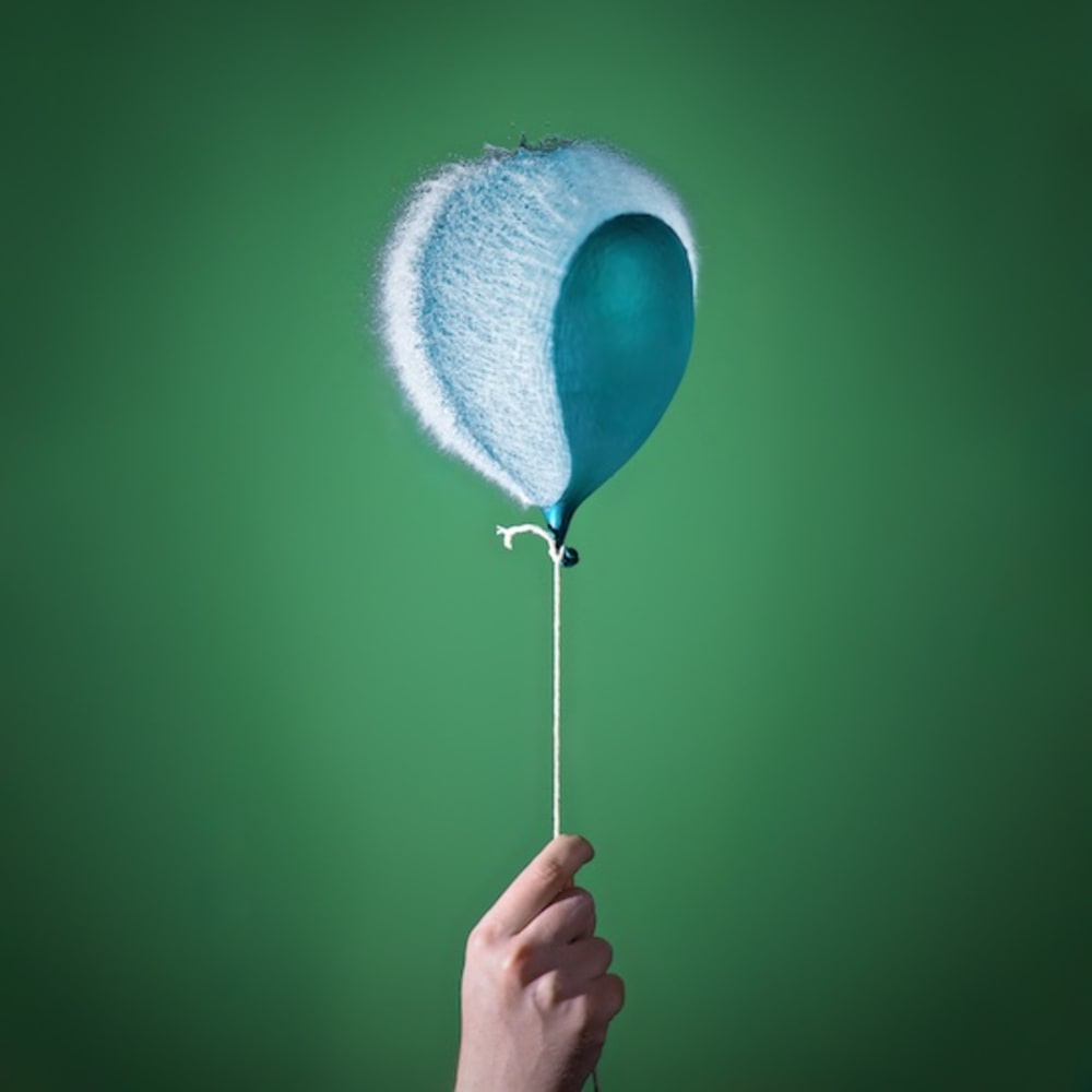 Photo of a water balloon bursting; it is attached to a string like a helium balloon.