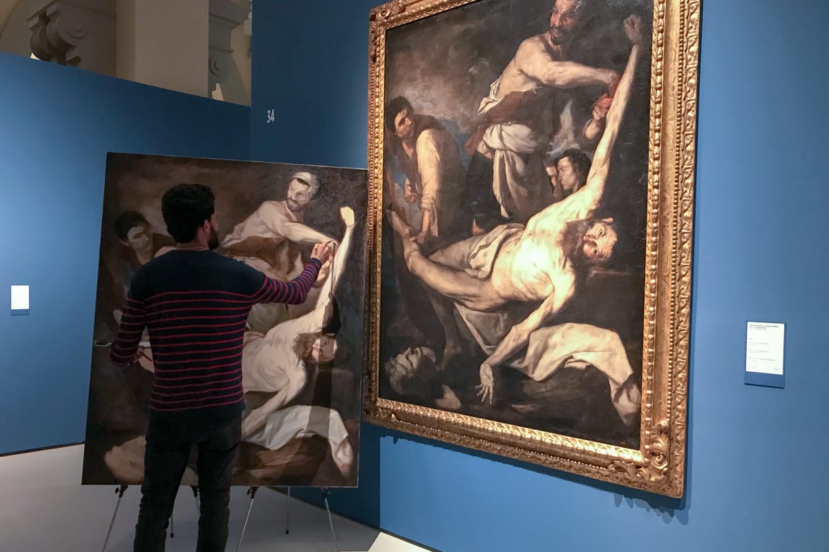 An artist painting a replica of a large oil painting hung on the wall.